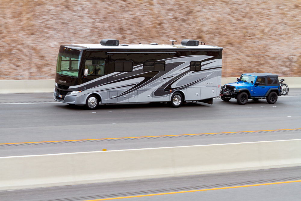 an RV towing a Jeep on the freeway - Shutterstock