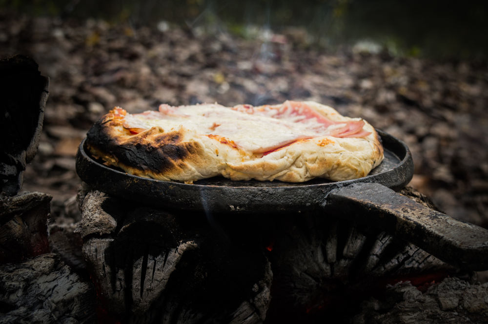 A pizza cooking over a campfire