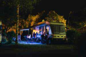 an RV awning lit up at night with people sitting underneath