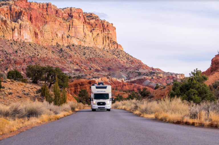 An RV driving down a road in front of red rocks