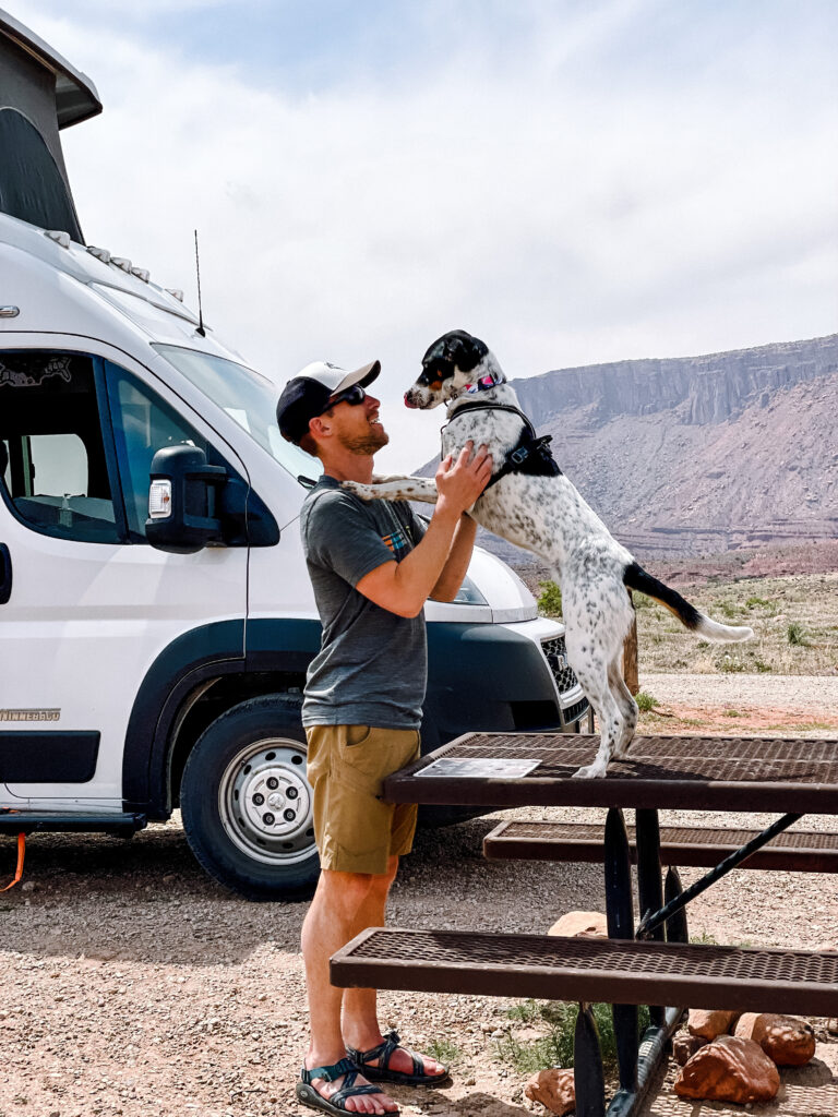 A man holding his dog next to a pop up camper