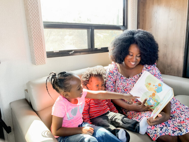 two girls reading books with their mom inside an RV