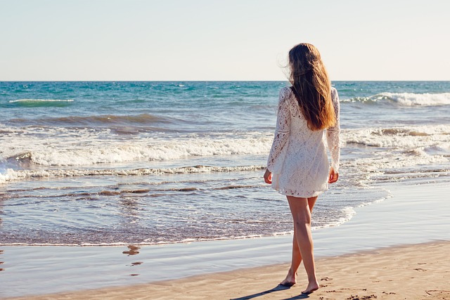 A woman walking towards the ocean on a sandy beach