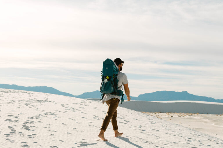 A man backpacking barefoot through the sand