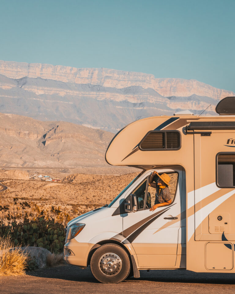 A person looking out the window of an RV in the desert