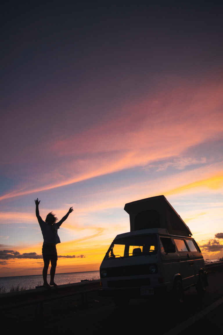 a person and RV campervan silhouetted against the setting sun