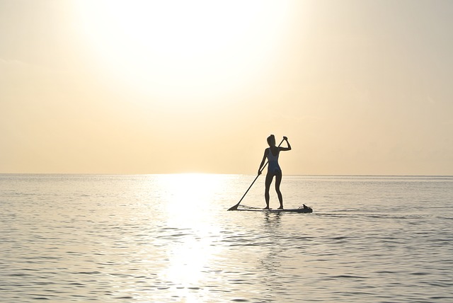 woman paddleboarding into the sunset