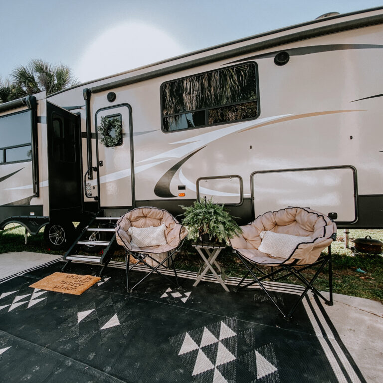 A travel trailer set up with chairs and a rug