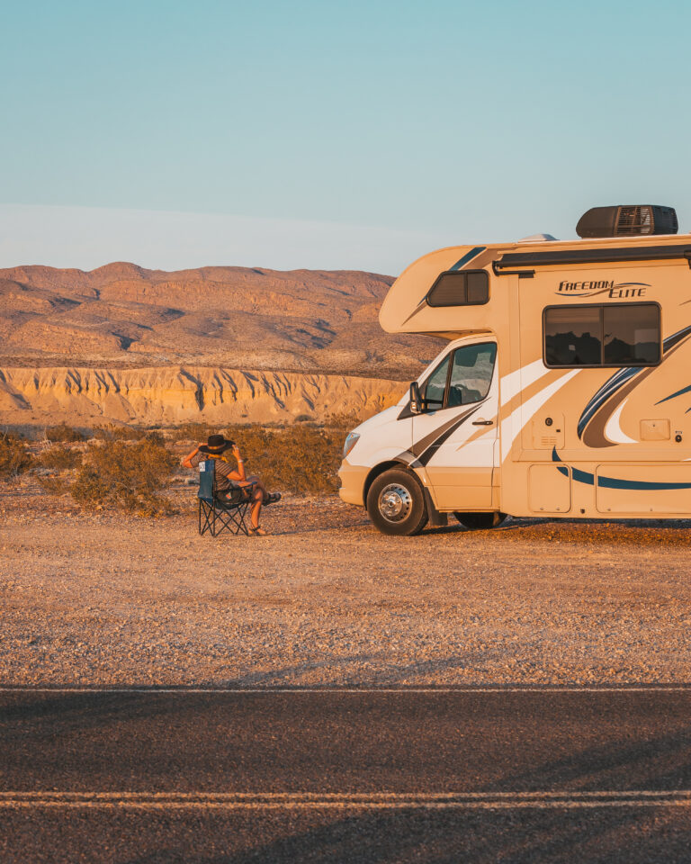 a person sitting next to an RV at sunset