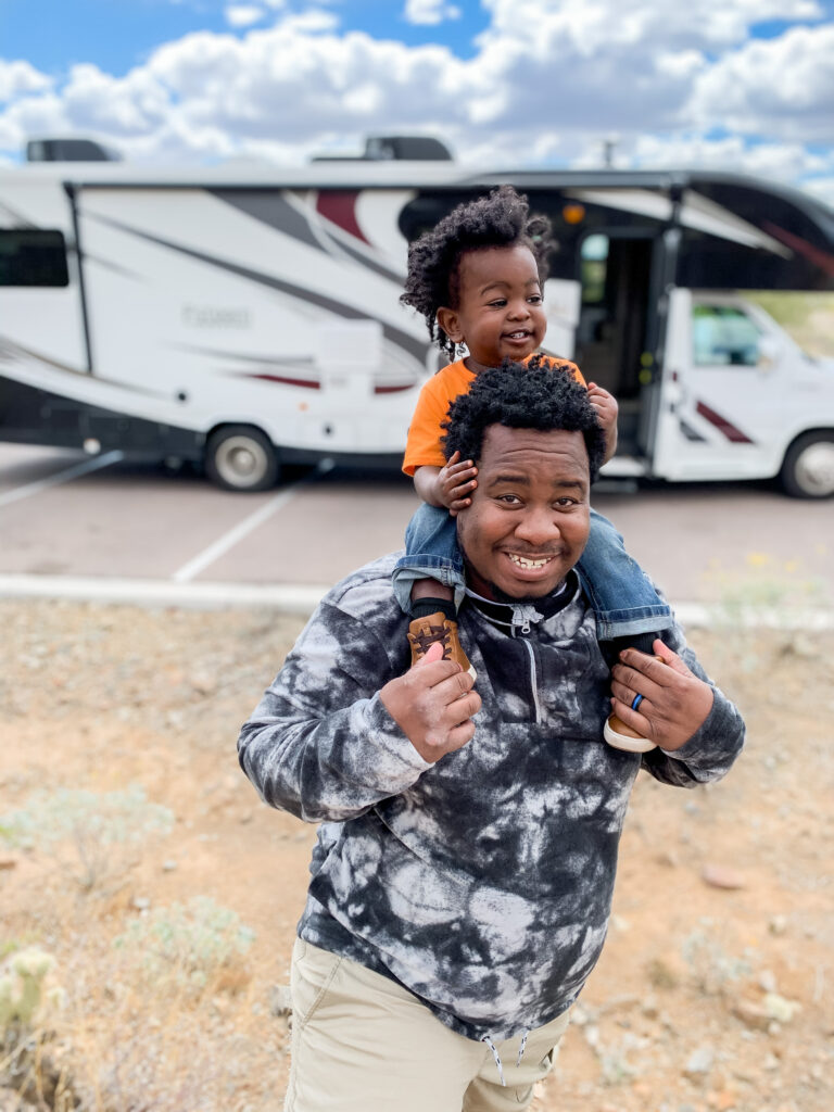 a dad with a child on his shoulders in front of his RV