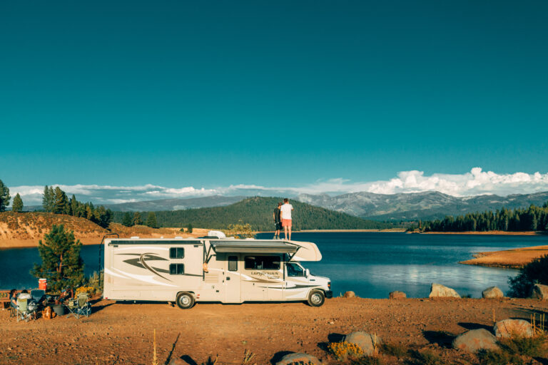 two men on the roof of an RV next to a lake