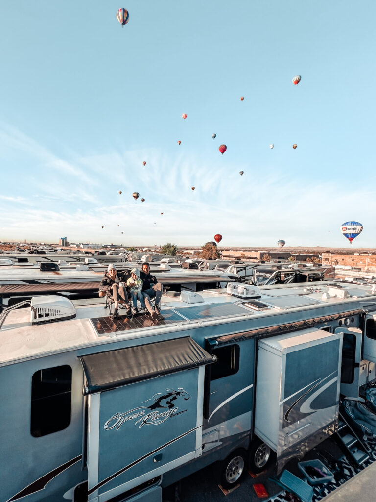 people sitting on top of their RV watching hot air balloons