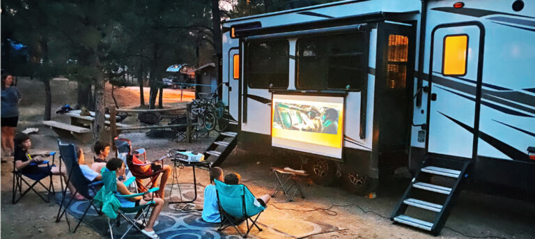 family watching a movie on a projector outside of an rv