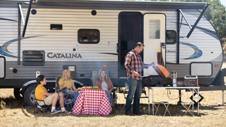 Family sitting around grill in front of travel trailer: the goal when learning about RVing for beginners