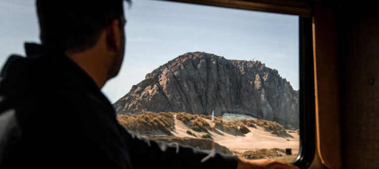 man looking out rv window and large rock formation