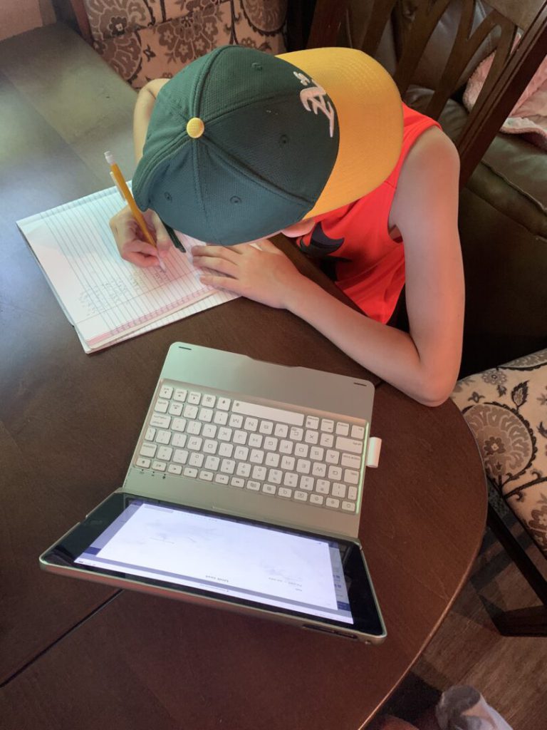 Boy slouches over notebook and laptop