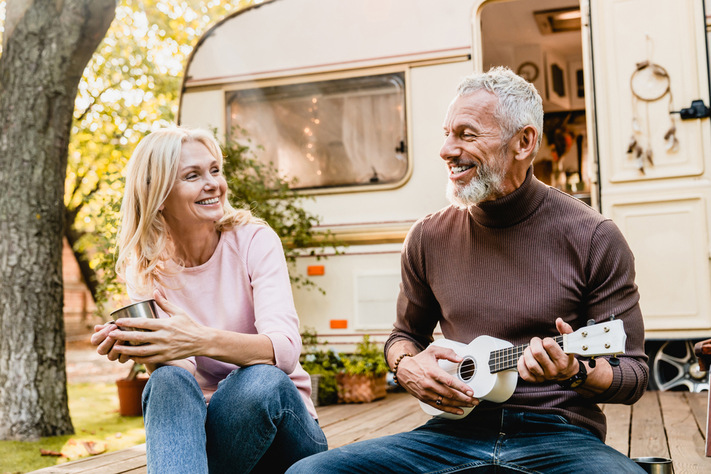 Mature man playing the ukulele for his wife near a campervan