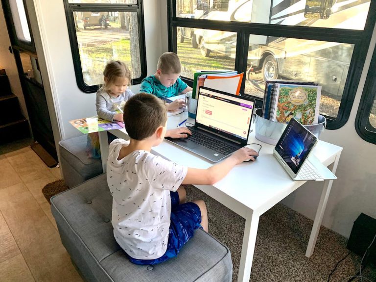 three children sit around a table on their computers during homeschool