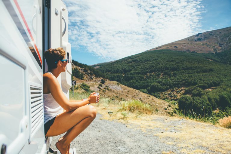 Young person sits on steps of RV and looks over a valley