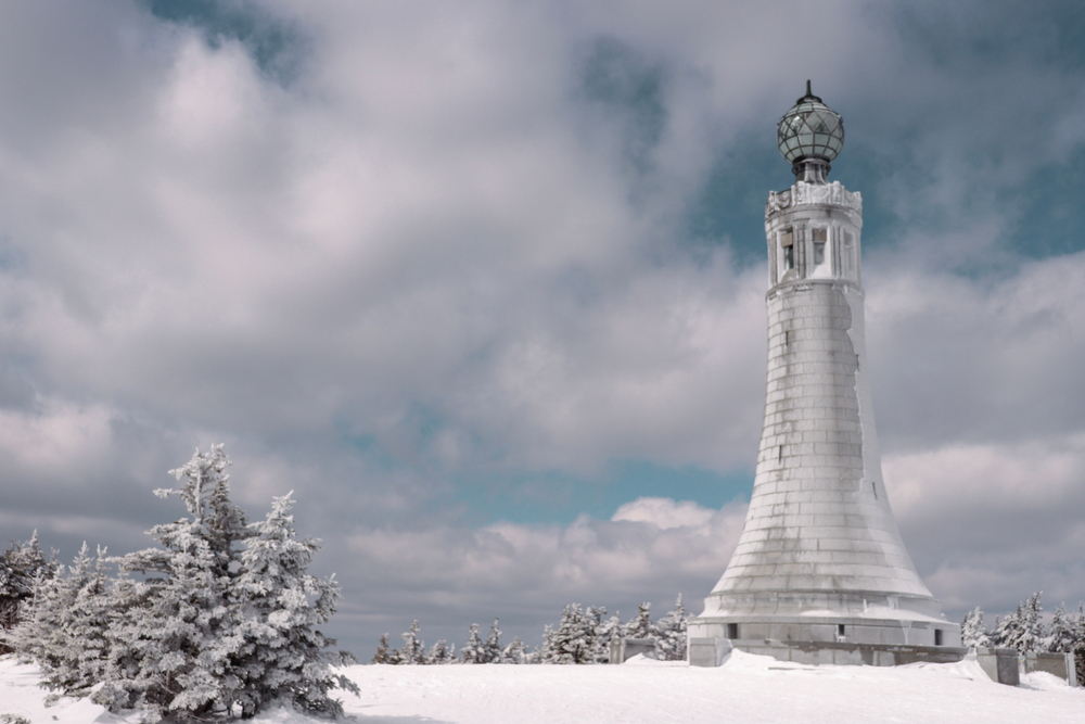 The top of Mount Greylock with Veterans Memorial at the summit in the winter next to the snowy trees.