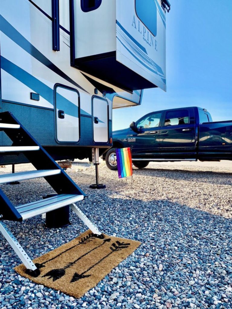 Exterior of a fifth-wheel trailer parked next to a truck with a rainbow pride flag