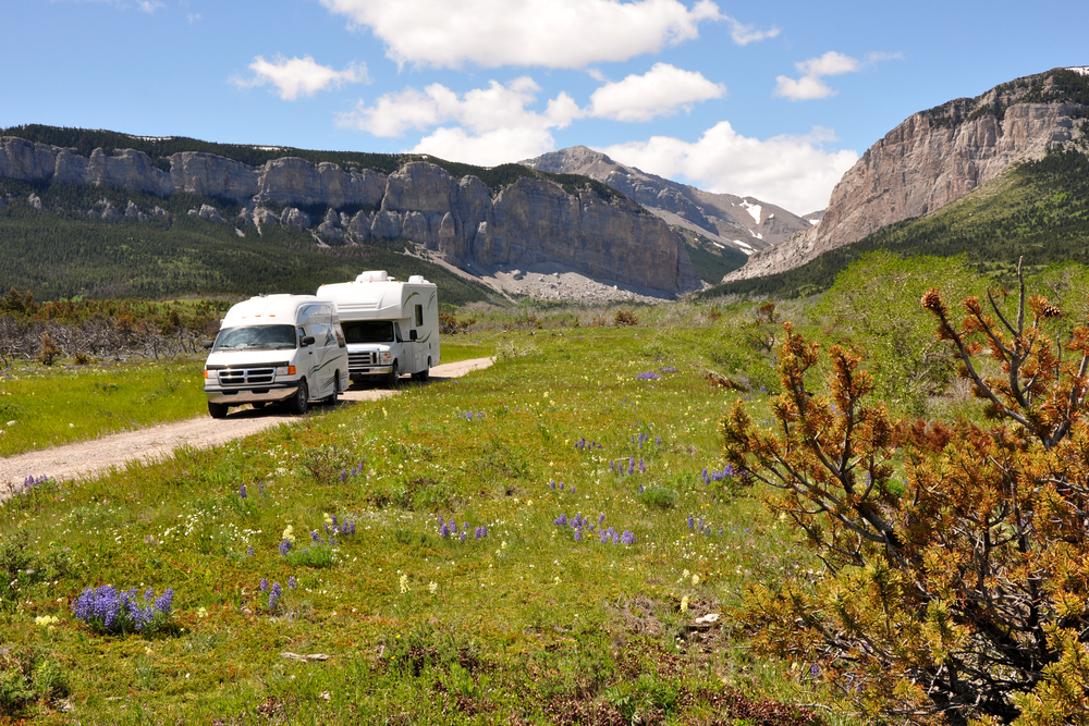 A camper van and an RV on a dirt road that runs from a grassy meadow to tall, rocky buttes