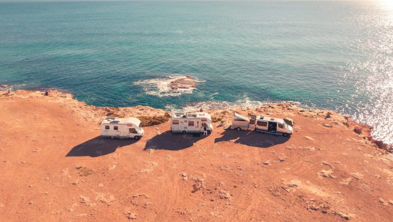 Three Class C RVs parked in a line along the coastline
