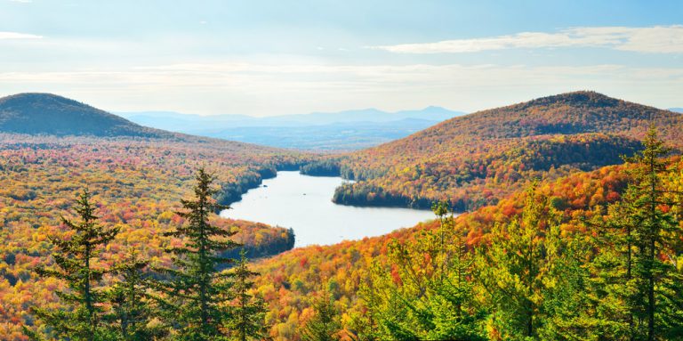 A lake sits in the middle of a valley full of autumn foliage, under a cloudy blue sky.