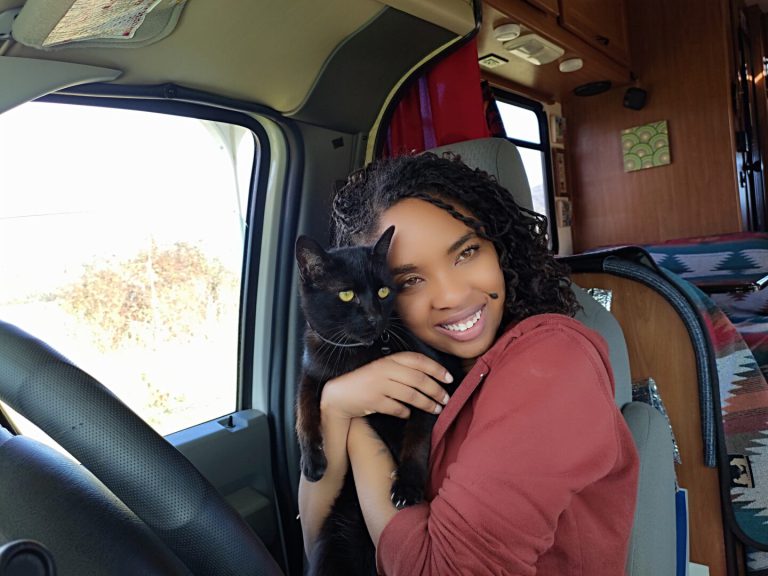 Young woman holds her cat seated at the wheel of her class c rv