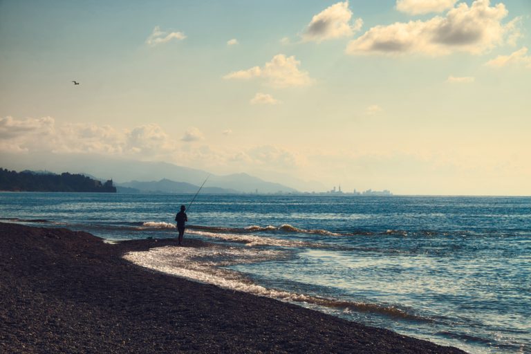 A person fishing on a beach while the waves rush toward the shore.