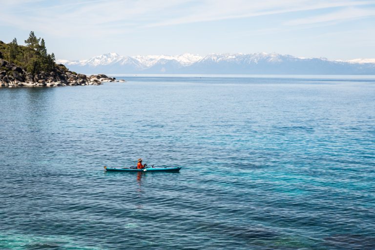 A person in fishing from a kayak on a large blue lake.