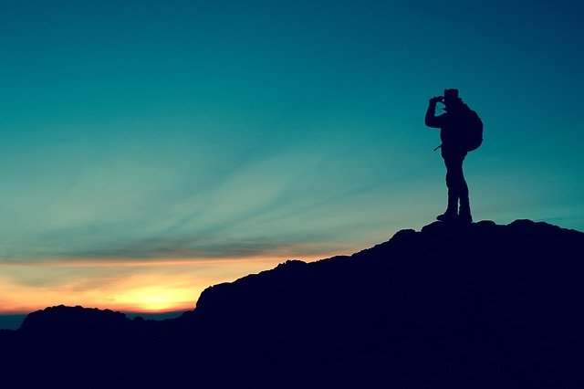 a hiker silhouetted against an evening sky with binoculars