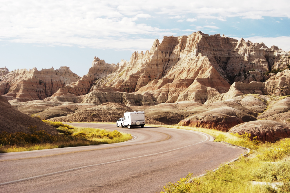 A vehicle pulls an RV on a curving road passing by unique rocky hills.