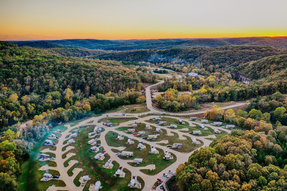 An aerial view of a large RV park with many sites nestled in a forest valley. 