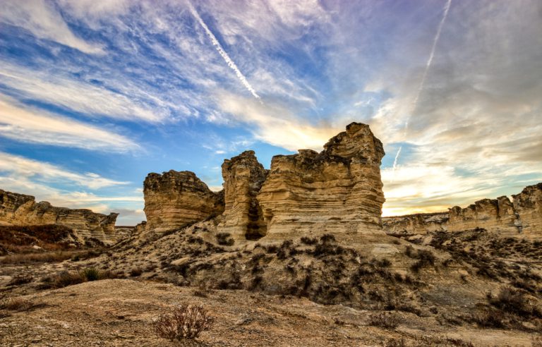 A unique rock formation with scrubby underbrush sits in a rocky plain,