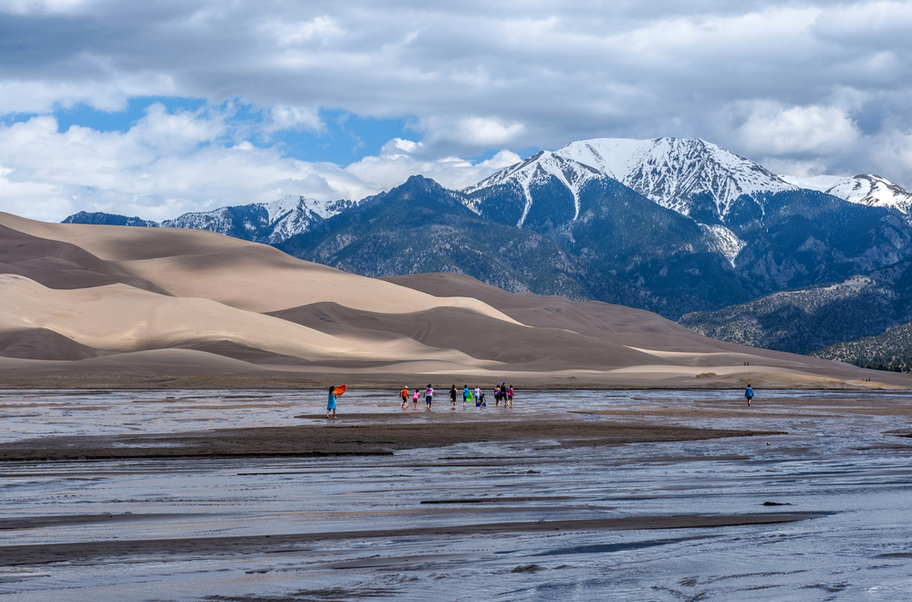 Great Sand Dunes National Park & Preserve, Colorado, USA - May 06, 2016: A group kids are playing in Medano Creek at the base of sand dunes and snow-capped peaks as spring clouds passing over.