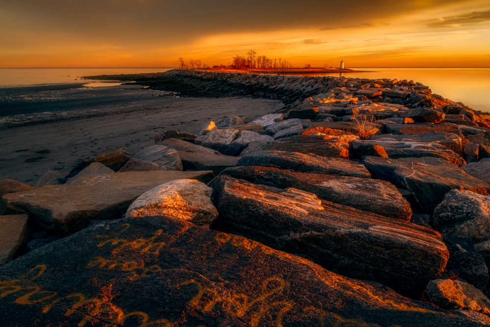The sun setting, turning the sky and water around a rocky breakwater orange.