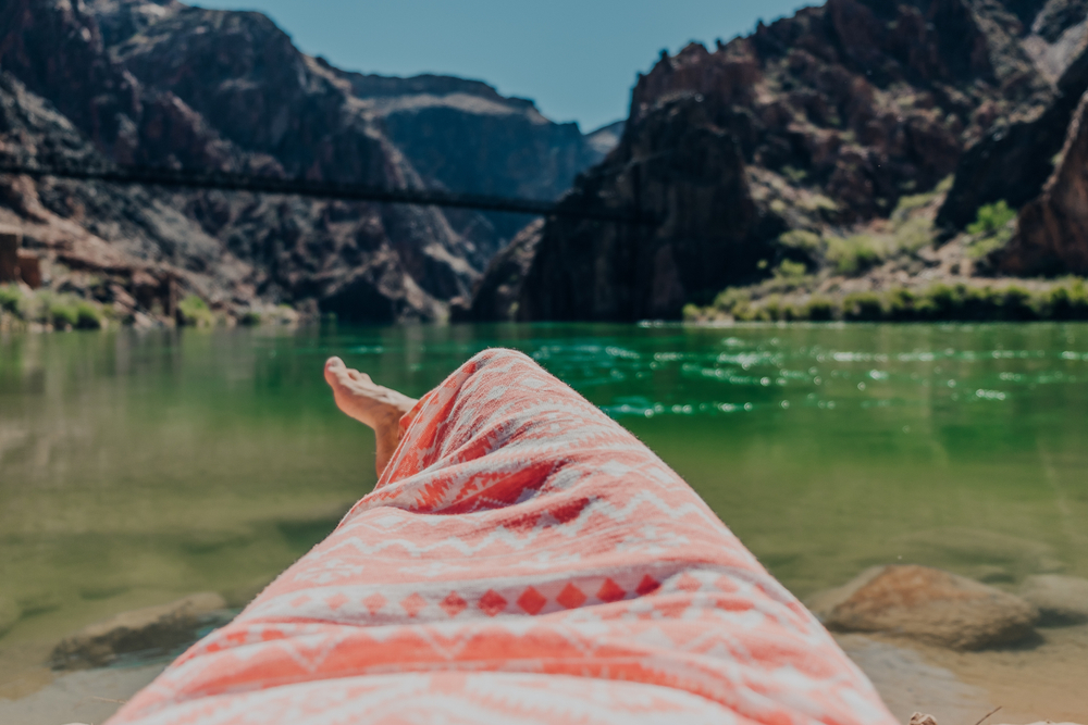 A girl in a dress resting on Boat Beach with a view of the green Colorado River in the Grand Canyon at Grand Canyon National Park in Arizona