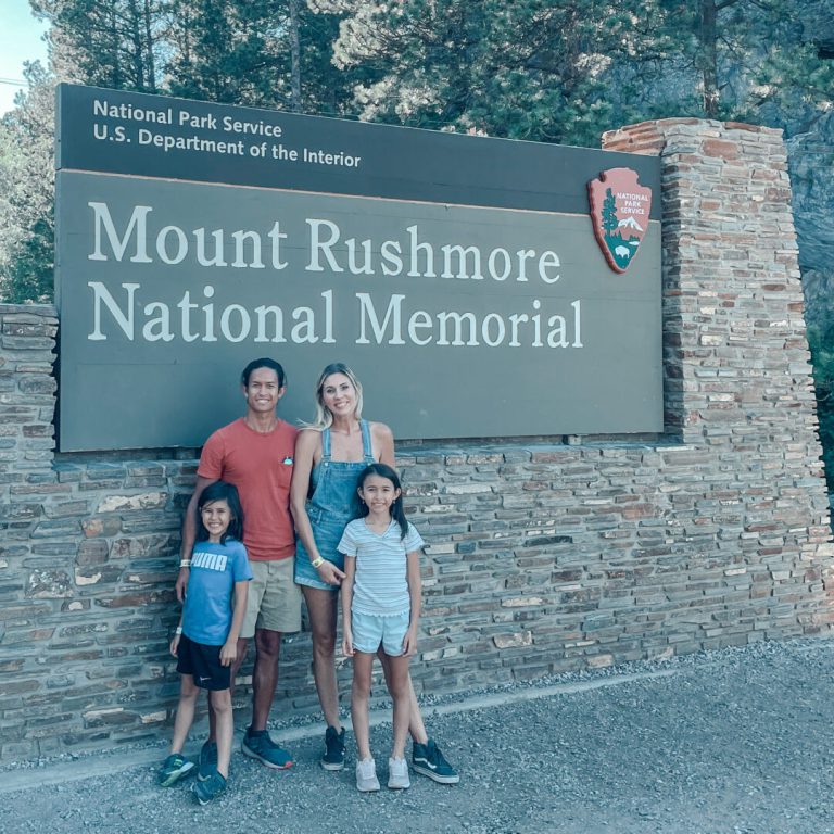 Family poses in front of Mount Rushmore National Memorial sign