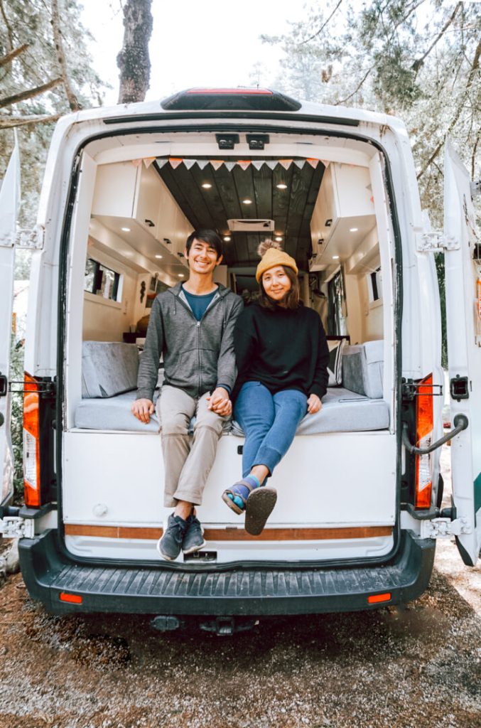 Young couple sits in the back of their campervan