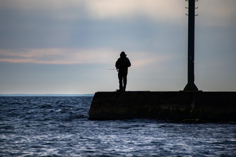 A silhouette of a fisherman fishing off a pier on a lake