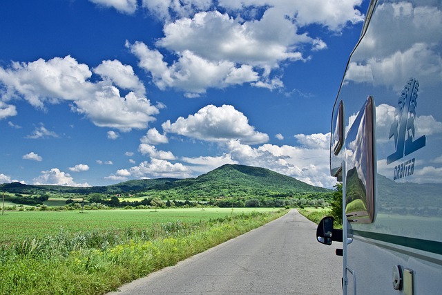 the side of an RV as it's driving down a road with blue skies and puffy clouds in the background