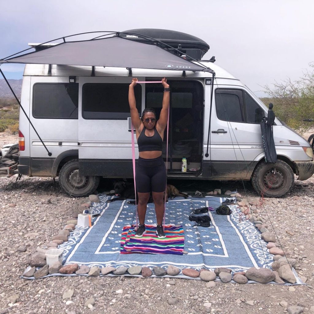Woman uses exercise band in front of her campervan