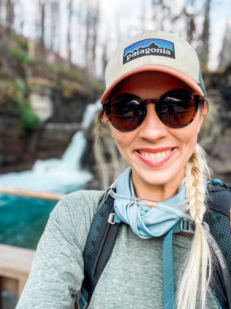 Woman smiles in front of waterfall at Glacier National Park