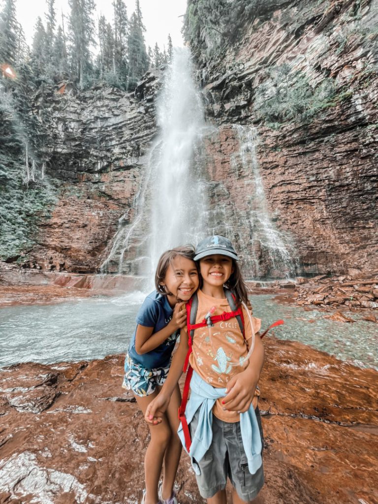 Two children smile in front of waterfall at Glacier National Park