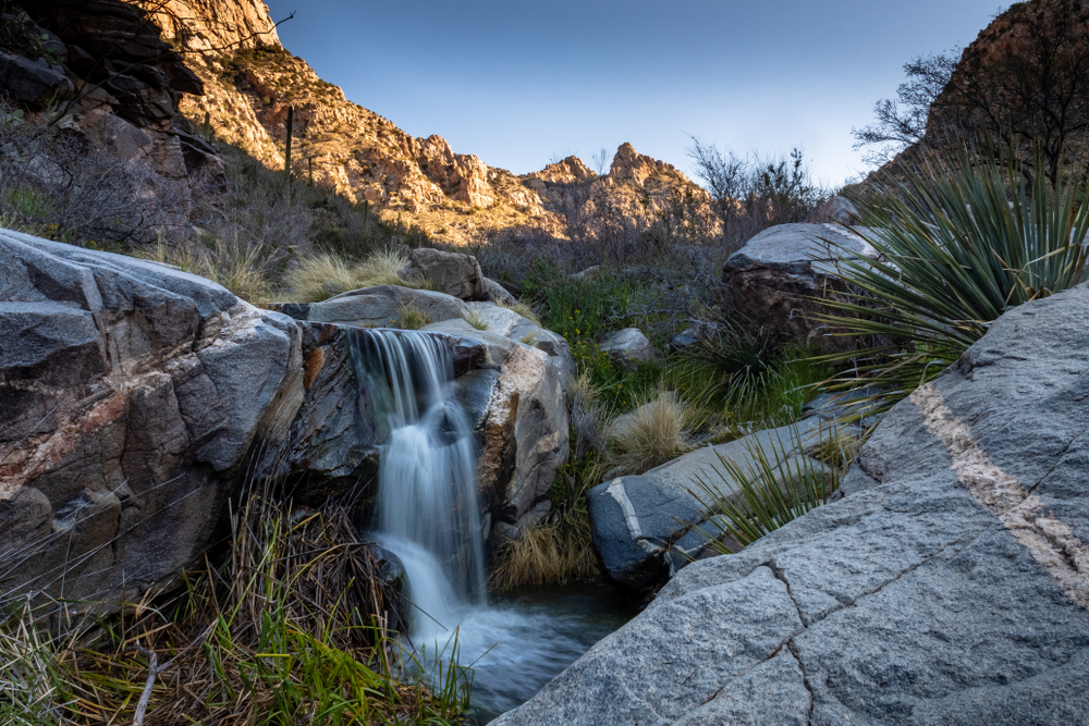 A waterfall along the beautiful Pima Canyon hiking trail in the Sonoran Desert. Southwestern landscape with blue sky, mountains, stone and running water. Catalina Mountains, Tucson, Arizona. 2019.