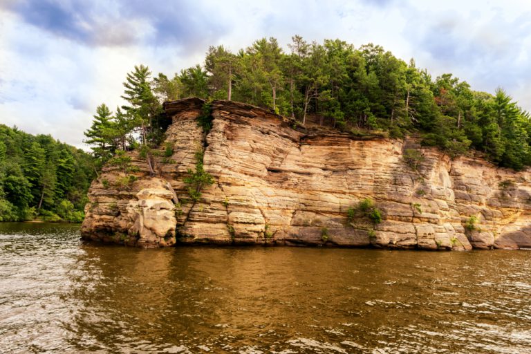 A river flows around a rock formation with trees growing on top of it.