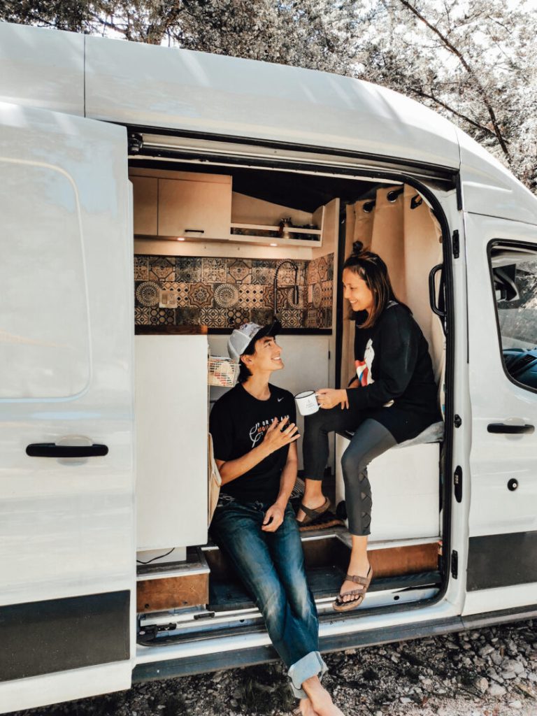 Couple drinks coffee inside the open door of their campervan