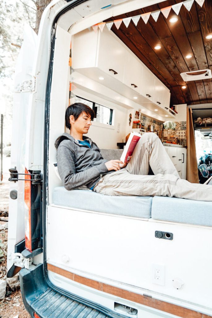 Man relaxes and reads on the bed of his campervan