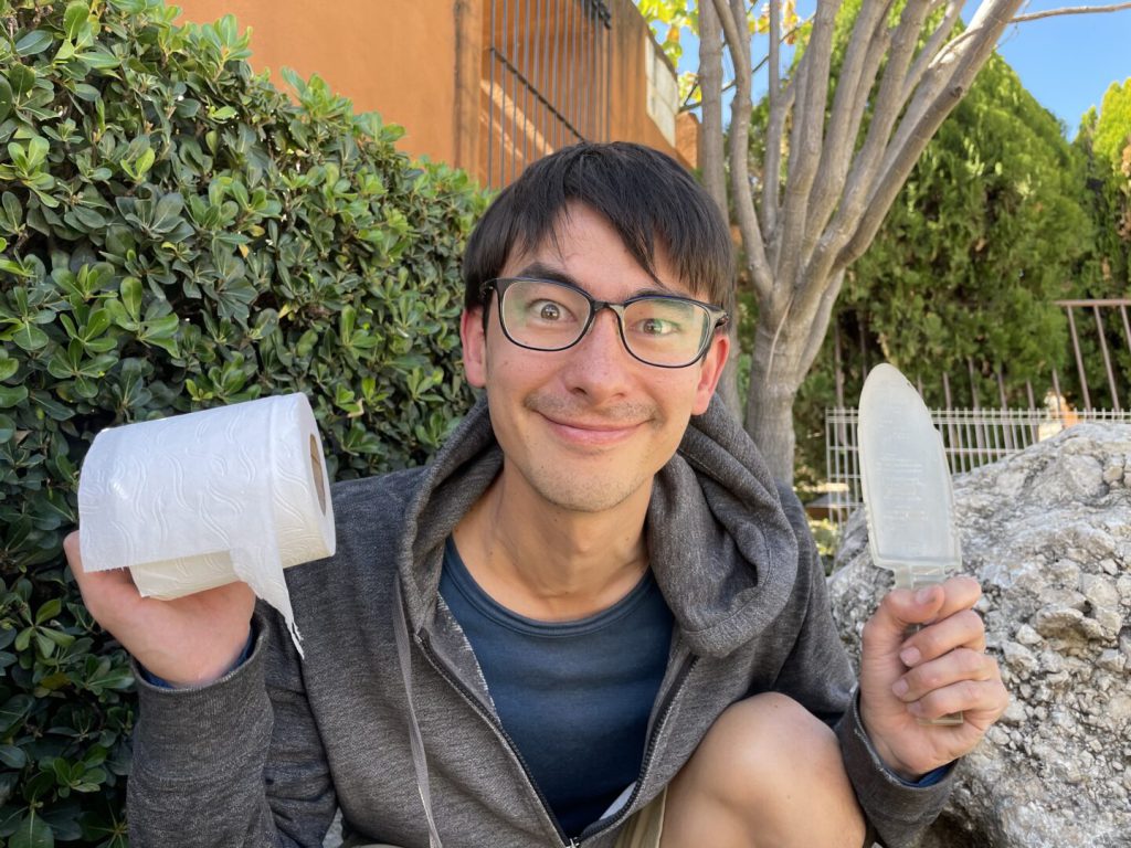 Man holds toilet paper and shovel while smiling